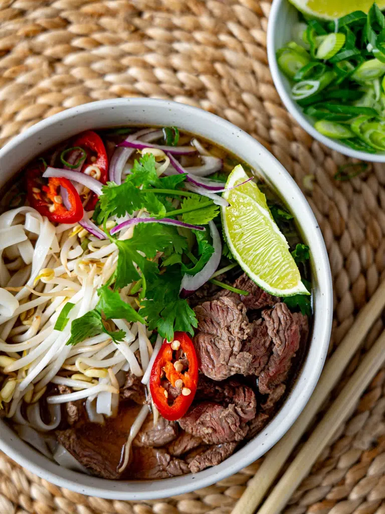 Overhead shot of Cheat's Beef Pho, featuring slices of beef, rice noodles, fresh herbs, and lime in a flavorful broth.