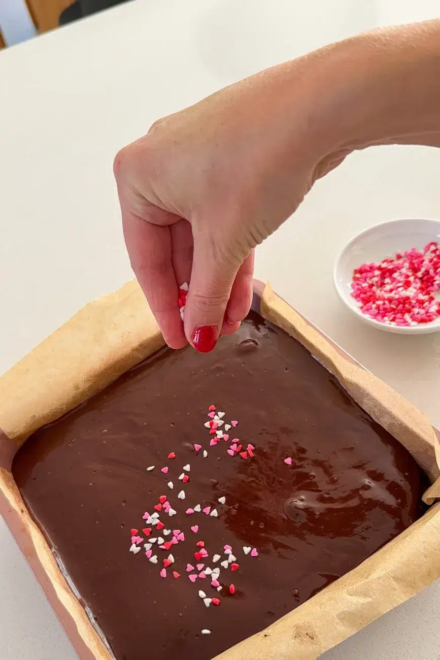 Chocolate ganache on brownie being finished with love heart sprinkles