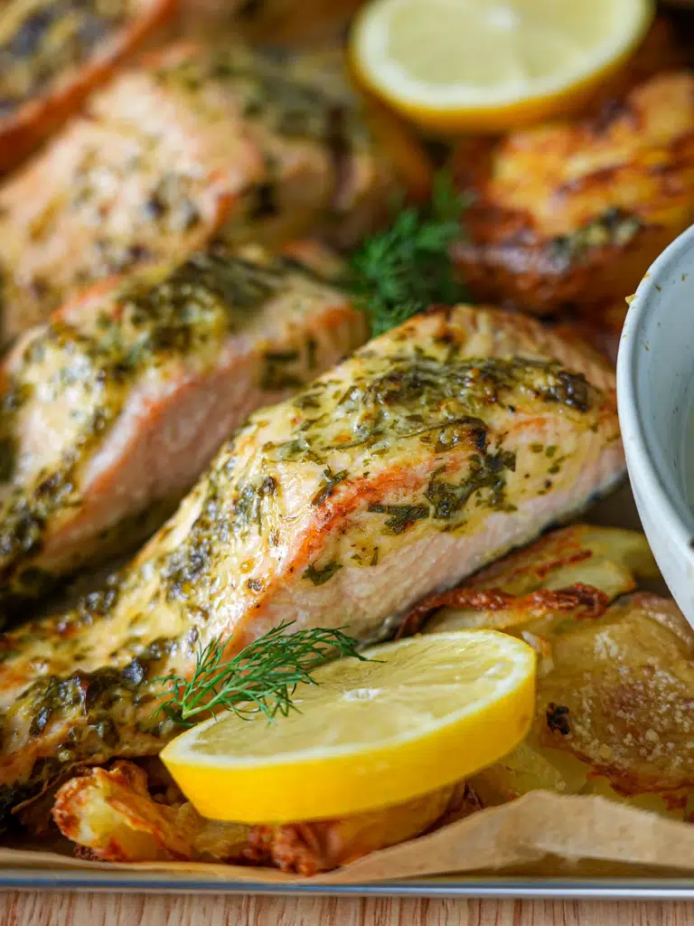 Dijon salmon fillet and roasted potatoes in a baking pan, garnished with herbs and a lemon slice