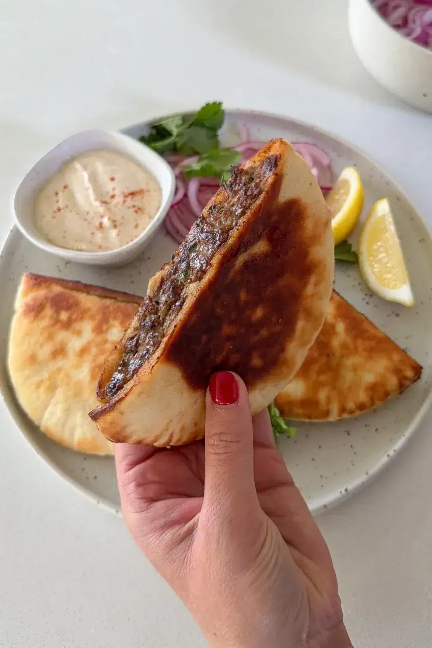 hands holding juicy stuffed pita arayes in kitchen