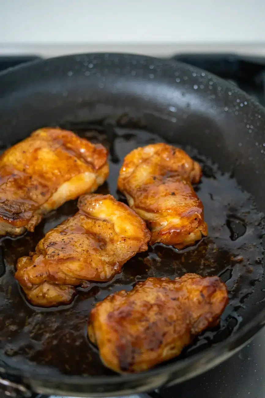 Chicken thighs simmering in a sweet and savory honey garlic sauce in a skillet.
