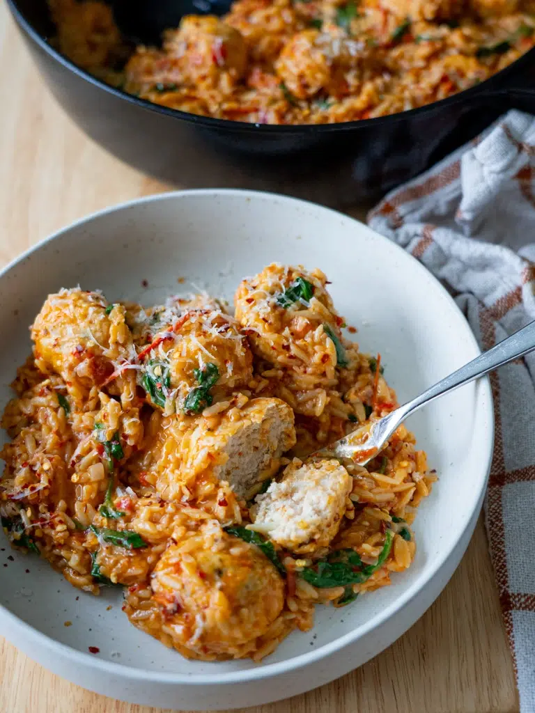 Plated Marry Me Chicken Meatballs in creamy sauce, with the pan in the background.