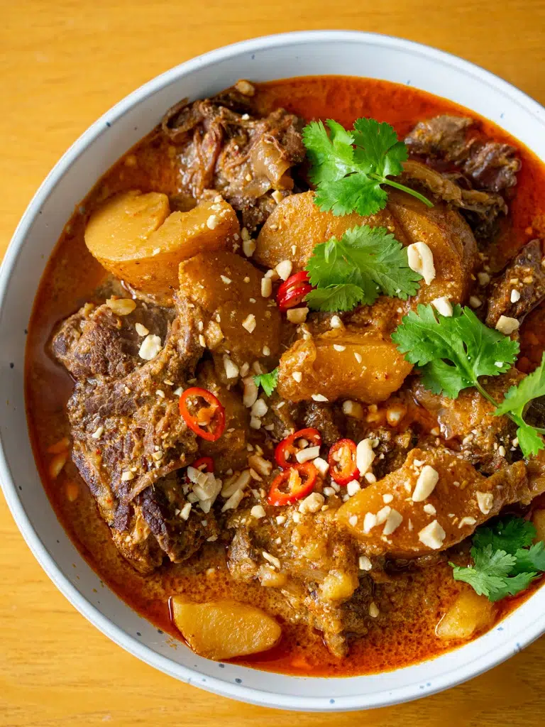 Top view of a big bowl of Massaman beef curry with potatoes in a rich, creamy sauce.