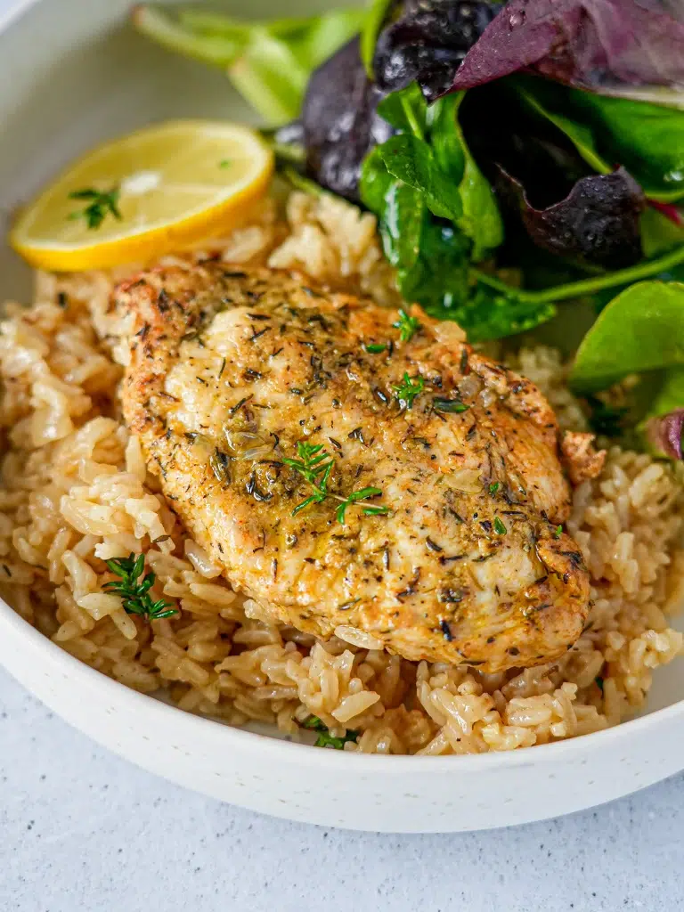 Bowl of lemon herb chicken and rice, showcasing tender chicken thighs garnished with fresh herbs and lemon slices, served over fluffy rice.