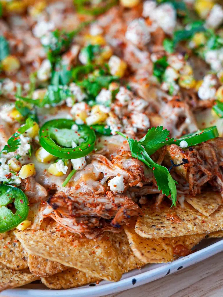 Close-up of Crispy nachos topped with golden melted cheese and a loaded corn topping.
