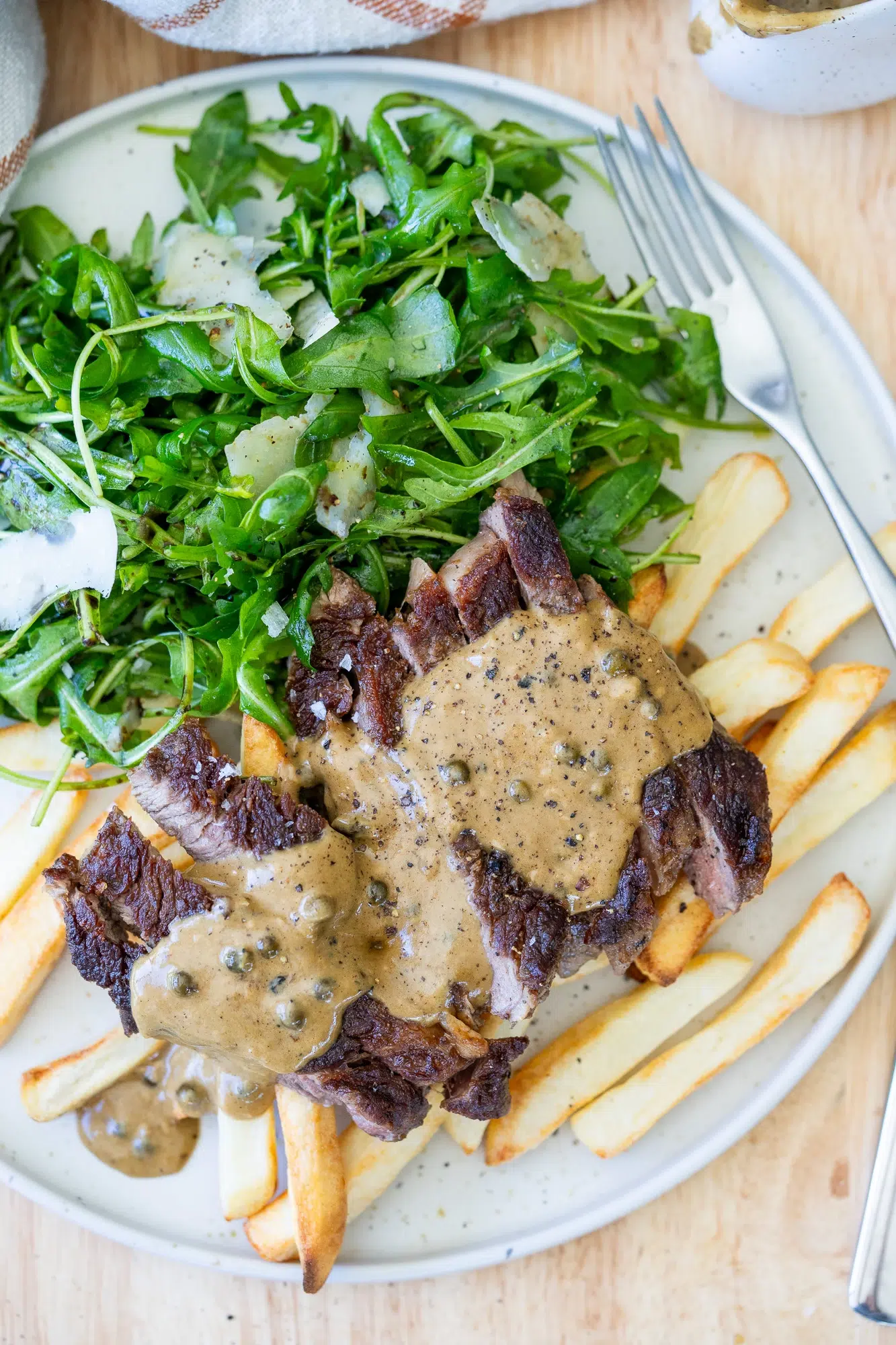 Plate of steak frites with peppercorn sauce and side of arugula salad with shaved parmesan